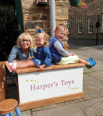 A woman and two children sitting on a wooden box with 'Harper's Toys' written on it
