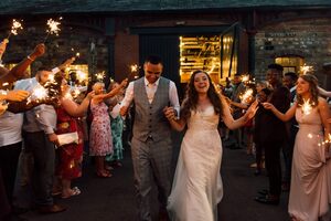 A bride and groom walking through the middle of their guests holding sparklers