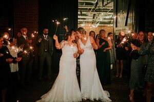 Two brides outside the ironworks with sparklers, surrounded by their guests also with sparklers.