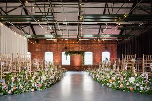 The Ironworks decorated for a wedding ceremony with wooden chairs decorated with foliage and a foliage arch at the top of the aisle