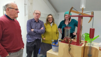 A small group of people observing how a steam engine works and functions.