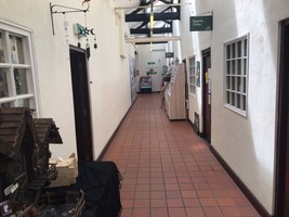 Craft and gift shop corridor. Red tiled floor with doors leading off either side and a wooden leaflet stand half way up.