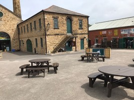 Circular brown picnic benches in the main courtyard at Elsecar. The antiques shop is to the right with historical adverts on the walls.