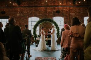 Two brides getting married under a foliage arch at the top of the ironworks
