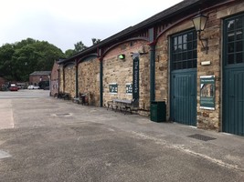 Exterior of the ironworks. A large stone building with green doors and a sign saying the iron works. Green wrought iron arches decorate the external walls.