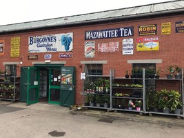 Elsecar Antiques centre entrance. A red brick building with a green door. Stands with pot plants on them are to the left and historical adverts such as Lyons Tea and Mazawattee tea on the wall.