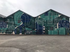 A large mural fully covering a wall. Greens and blues showing cogs and wheels representing Elsecar's industrial heritage.